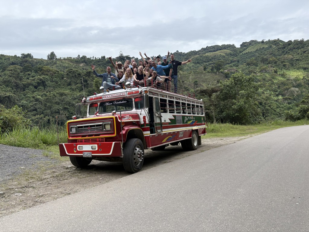 22-35ers reis Colombia: groep reizigers op het dak van een kleurrijke bus in de groene bergen.