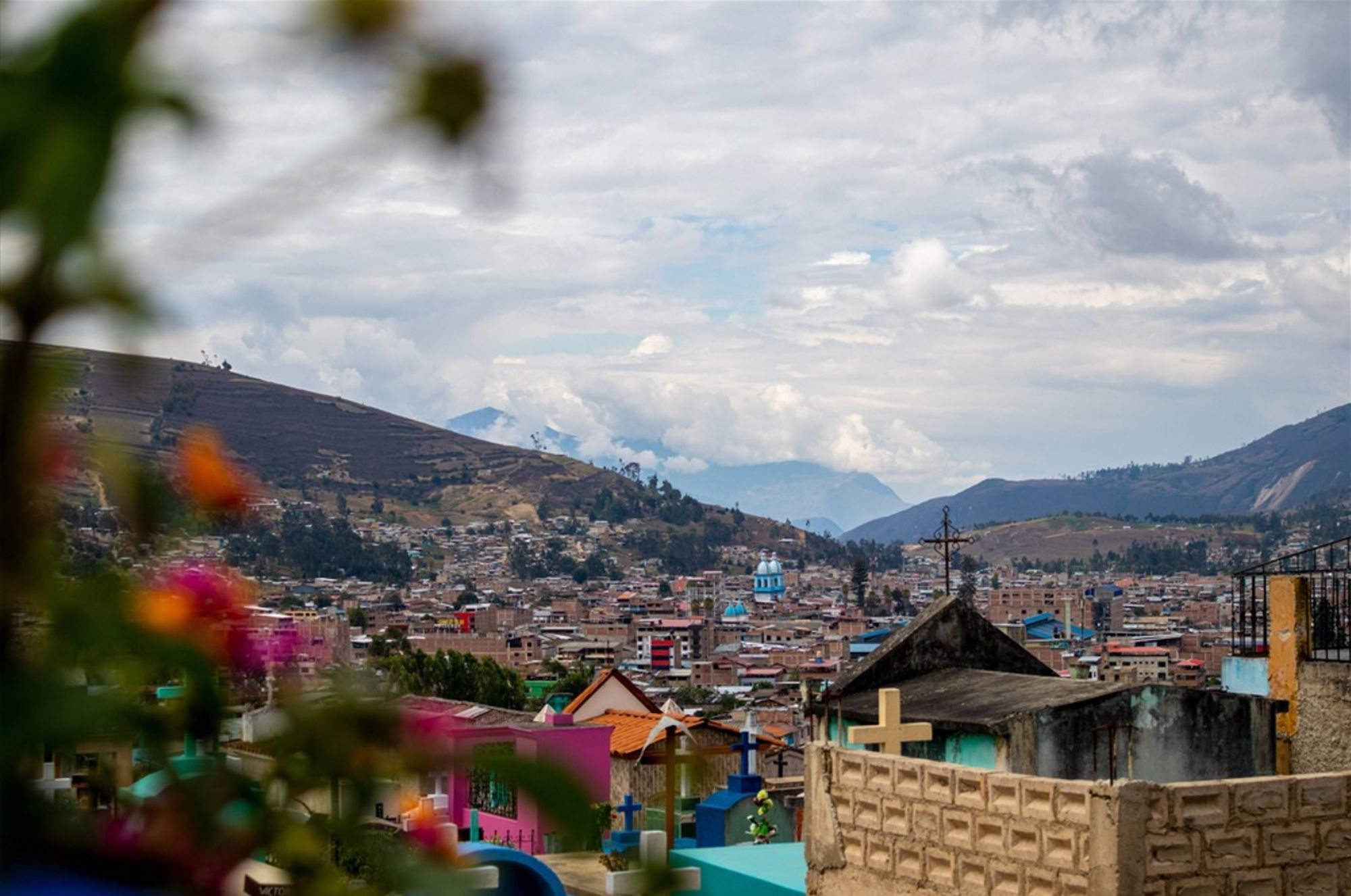 Uitzicht over een stad in de Peruaanse Andes met kleurrijke graven op de voorgrond en bergen onder bewolkte lucht.