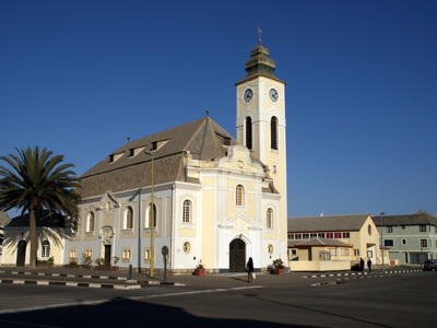 Christuskirche in Windhoek, Namibië, met klokkentoren en palmbomen onder een heldere blauwe lucht.