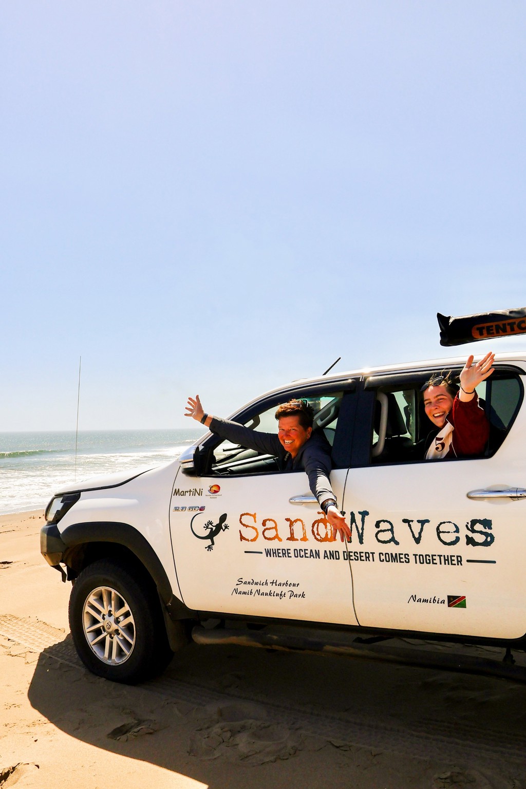 Reizigers in 4x4 bij Sandwich Harbour, Namibië, waar oceaan en woestijn samenkomen tijdens kampeerreis.