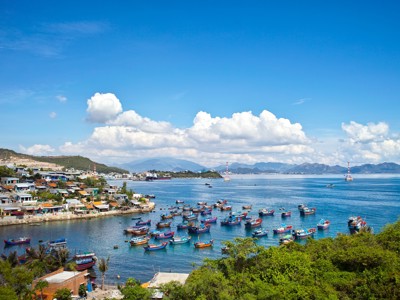 Uitzicht op een Vietnamese vissershaven met kleurrijke boten in de baai en bergen op de achtergrond.