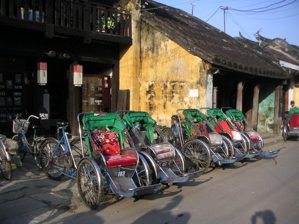 Riksja’s langs een straat met oude gele gebouwen in Vietnam tijdens een 22-35ers groepsreis.