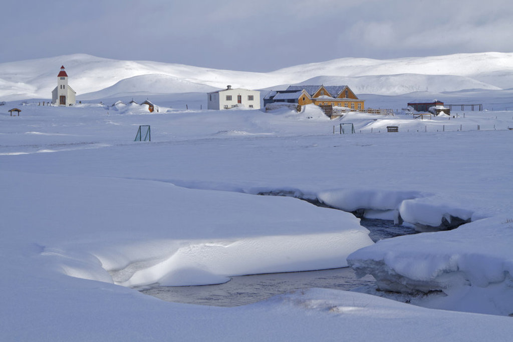 Sneeuwlandschap in Noord-IJsland met een kerk en boerderijen bij een deels bevroren rivier.