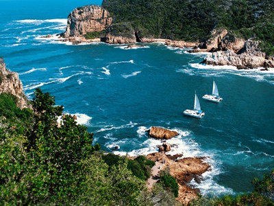 Uitzicht op de kust bij Knysna aan de Tuinroute, met zeilboten op zee en rotsachtige kliffen.