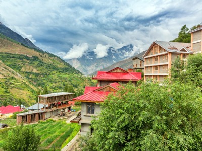 Bergdorp in de Spiti-vallei met rode daken, groene terrassen en besneeuwde toppen onder wolken.