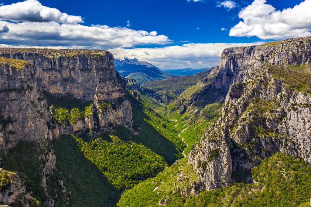 Uitzicht over de Vikos-kloof in Griekenland met steile rotswanden en groene vallei onder een blauwe lucht.