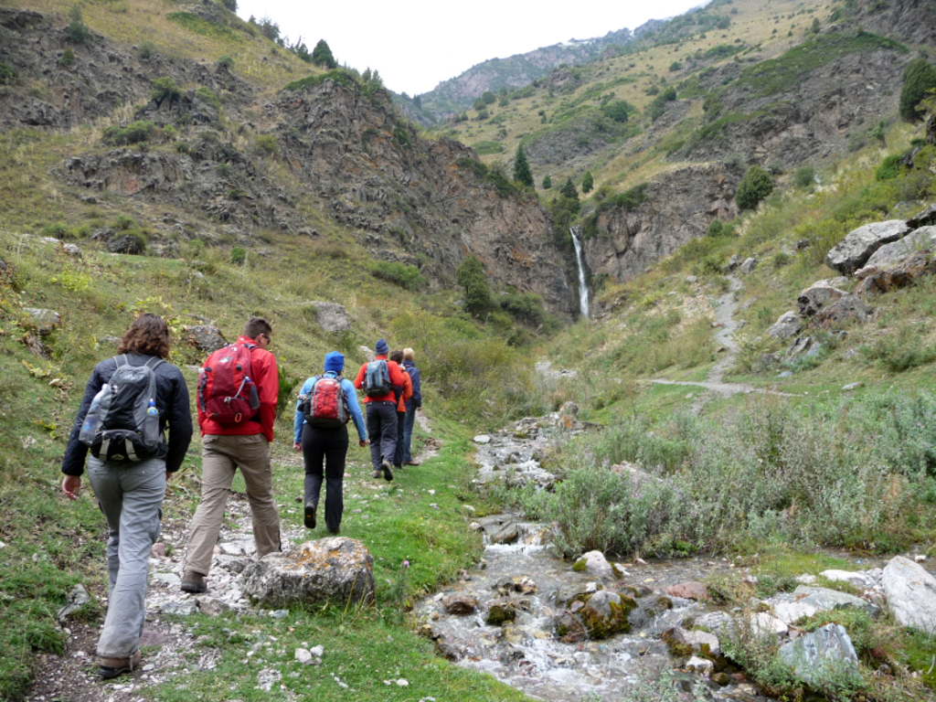 Wandelaars tijdens groepsrondreis Kirgistan in een bergkloof, langs een beekje met waterval.
