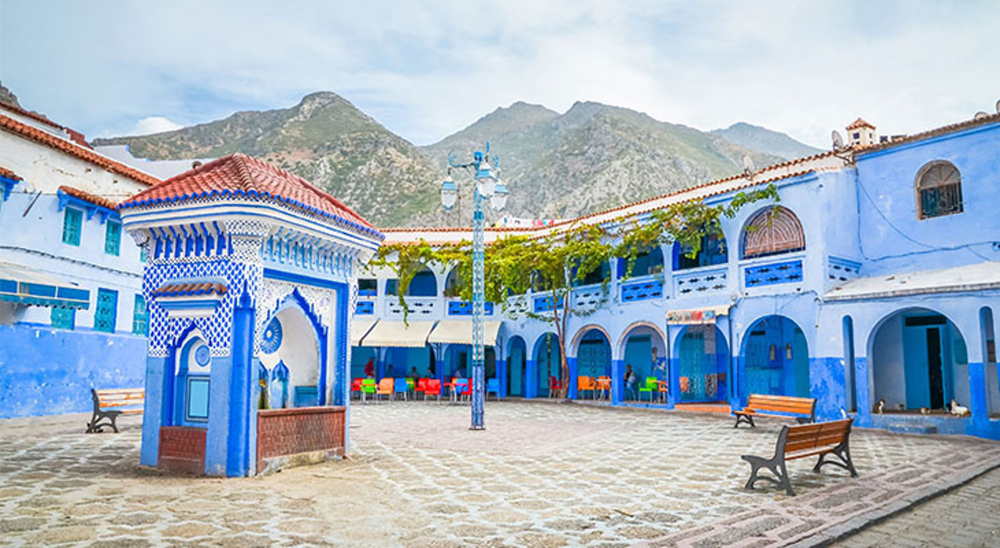Blauw-witte binnenplaats met mozaïekfontein in Chefchaouen, Marokko, met het Rifgebergte op de achtergrond.
