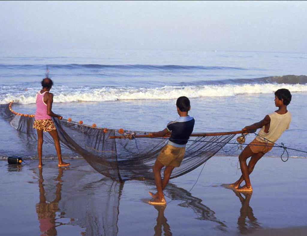 Vissers halen een groot visnet binnen aan het strand in Zuid-India, met golven op de achtergrond.