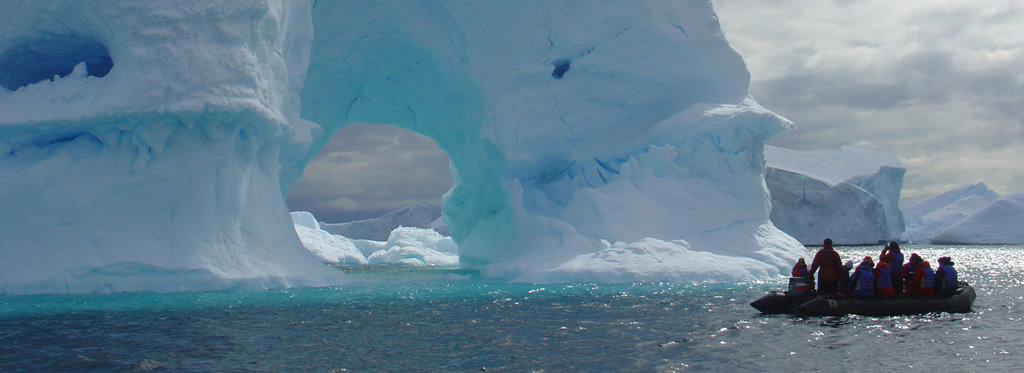 Zodiacboot met reizigers langs een imposante ijsberg in Antarctica tijdens groepsrondreis per vliegtuig.