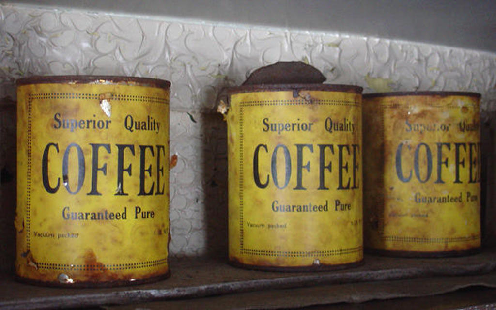 Oude koffiebussen met het opschrift “Superior Quality Coffee” op een plank.