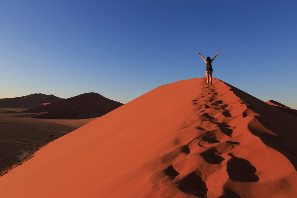 Reiziger op een rode zandduin in Namibië met armen omhoog tijdens 22-35ers reis Zuidelijk Afrika.