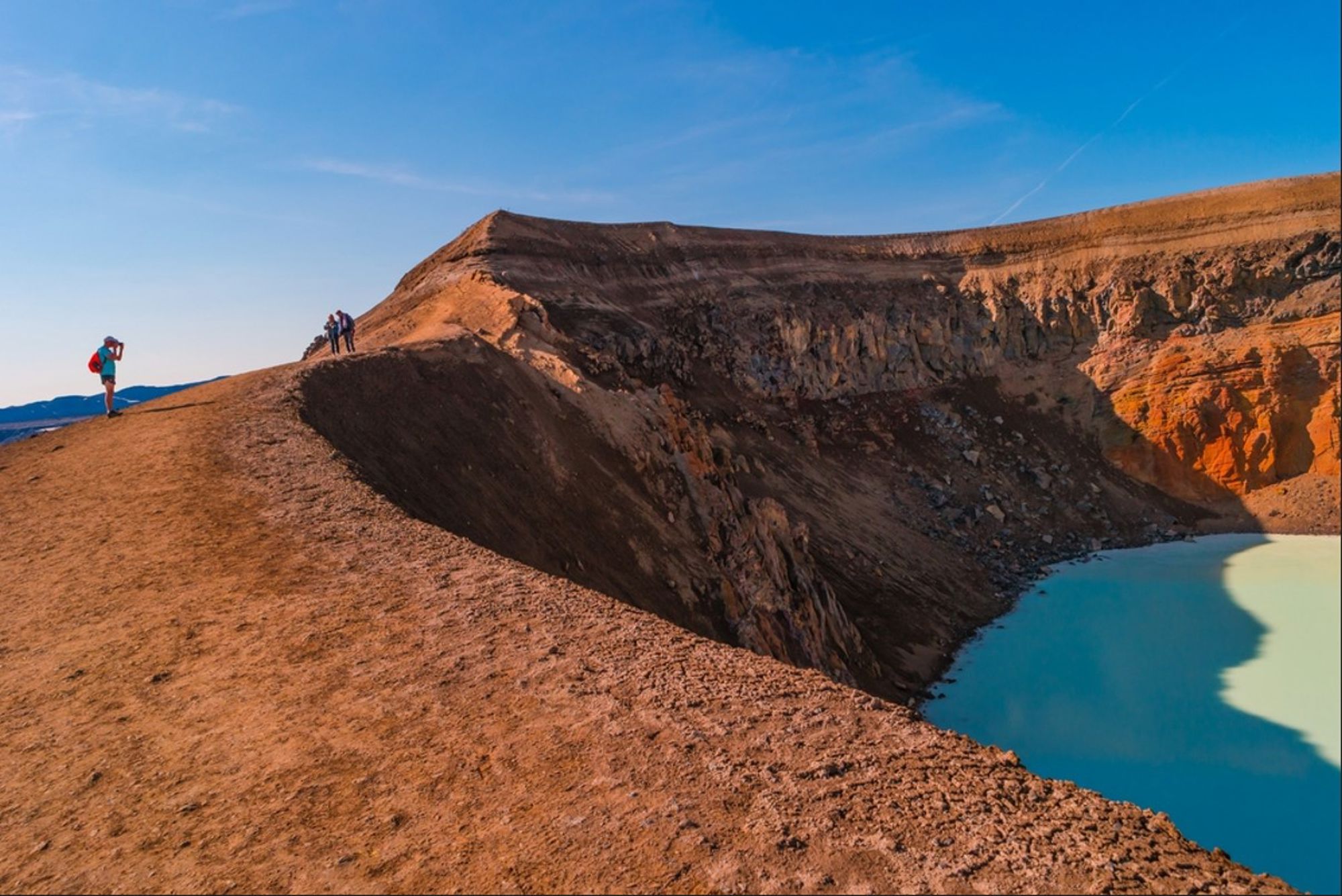 Wandelaars op de rand van de Víti-krater met het blauwgroene kratermeer bij Krafla in IJsland.