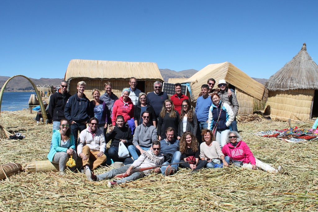 Groepsfoto van reizigers tijdens een groepsrondreis Peru bij rieten hutten op het Titicacameer.