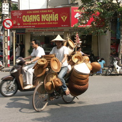 Straatbeeld in Vietnam met fietser die rieten manden en hoeden vervoert tijdens een fietsvakantie.