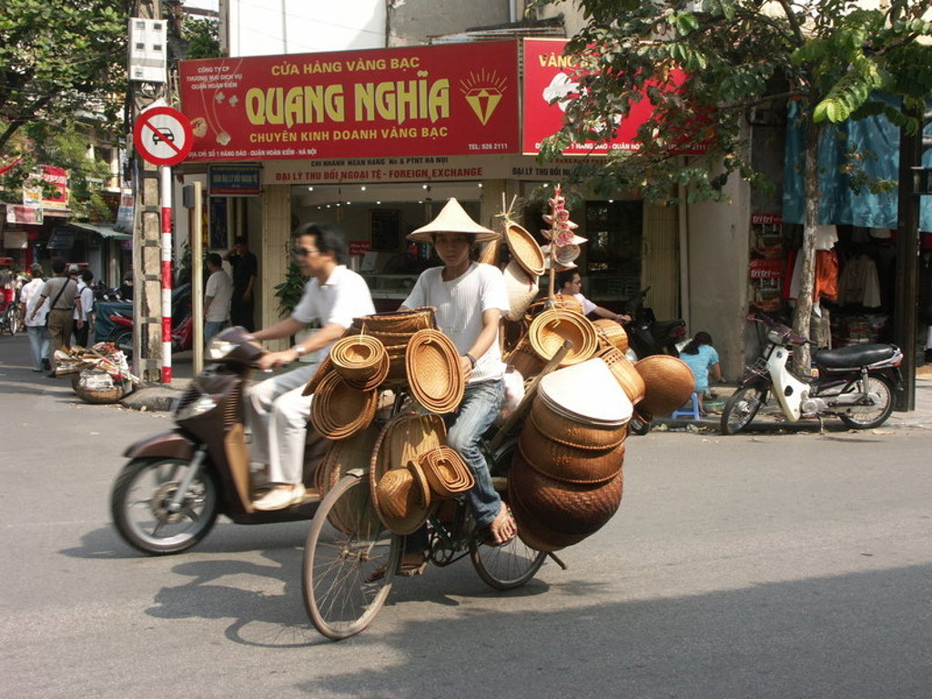 Straatbeeld in Vietnam met fietser die rieten manden en hoeden vervoert tijdens een fietsvakantie.