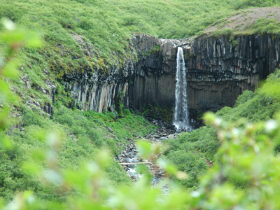 Waterval in groene kloof met basaltkolommen langs de Route IJsland.