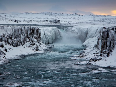 Besneeuwde waterval en kloof in Noord-IJsland, met stromende rivier tussen ijsranden.