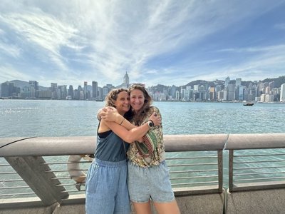 Twee reizigers omhelzen elkaar aan de Victoria Harbour met de skyline van Hongkong op de achtergrond.