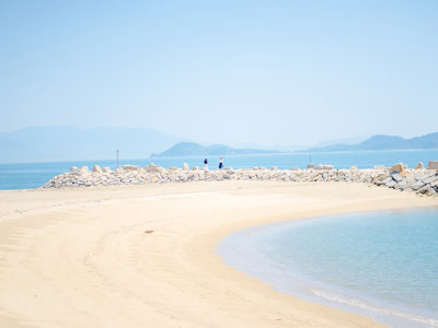 Zandstrand met rustige baai en rotsdam aan de Japanse kust, met bergen op de achtergrond.