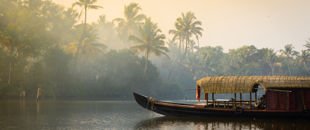 Traditionele houseboat op de backwaters van Zuid-India bij zonsopkomst, omringd door palmbomen.