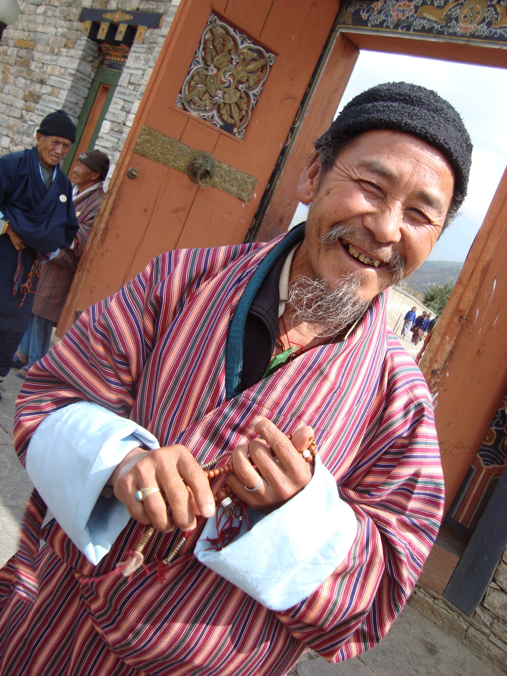 Lachende man in traditionele Bhutaanse kleding bij een kloosterpoort tijdens groepsrondreis Sikkim en Bhutan.
