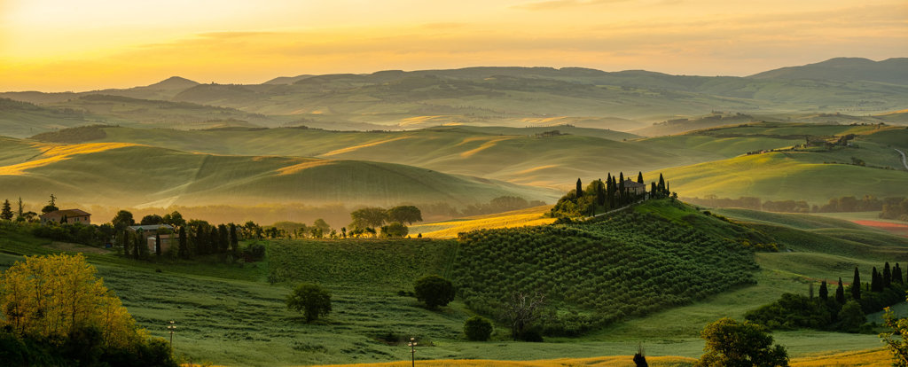 Glooiende heuvels en cipressen in Toscane bij zonsondergang tijdens een fietsvakantie.