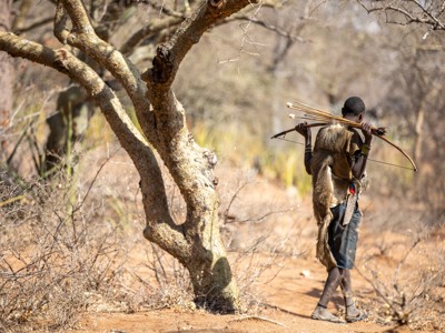 Hadzabe-jager met boog en pijlen loopt door de savanne in Tanzania tijdens de route Kenia en Tanzania.