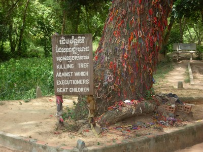 Killing Tree bij Choeung Ek, Phnom Penh, met kleurrijke armbandjes en herdenkingsbord.