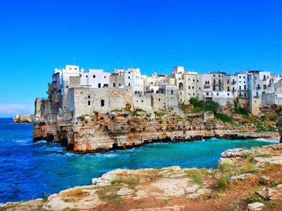 Witte huizen op kliffen aan de Adriatische kust in Puglia, Italië, met helderblauwe zee en lucht.
