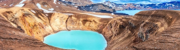 Turquoise kratermeer in de Askja-vulkaan, omringd door ruige lavavelden en besneeuwde bergkammen in IJsland.