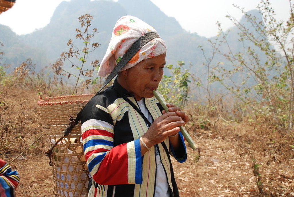 Vrouw in traditionele kleding speelt bamboefluit in het berglandschap van Thailand tijdens een groepsrondreis.
