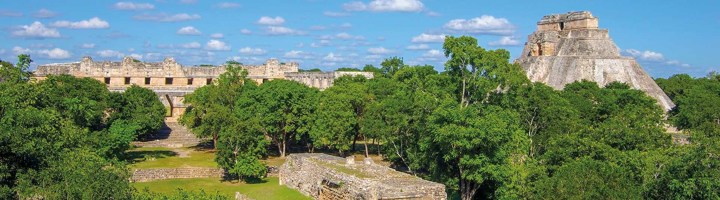 Maya-ruïnes van Uxmal in Mexico, omringd door jungle en onder een blauwe lucht.