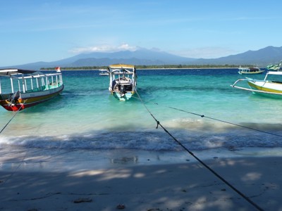 Bootjes voor anker in azuurblauwe zee bij Gili Air, met Lombok en vulkanen op de achtergrond.