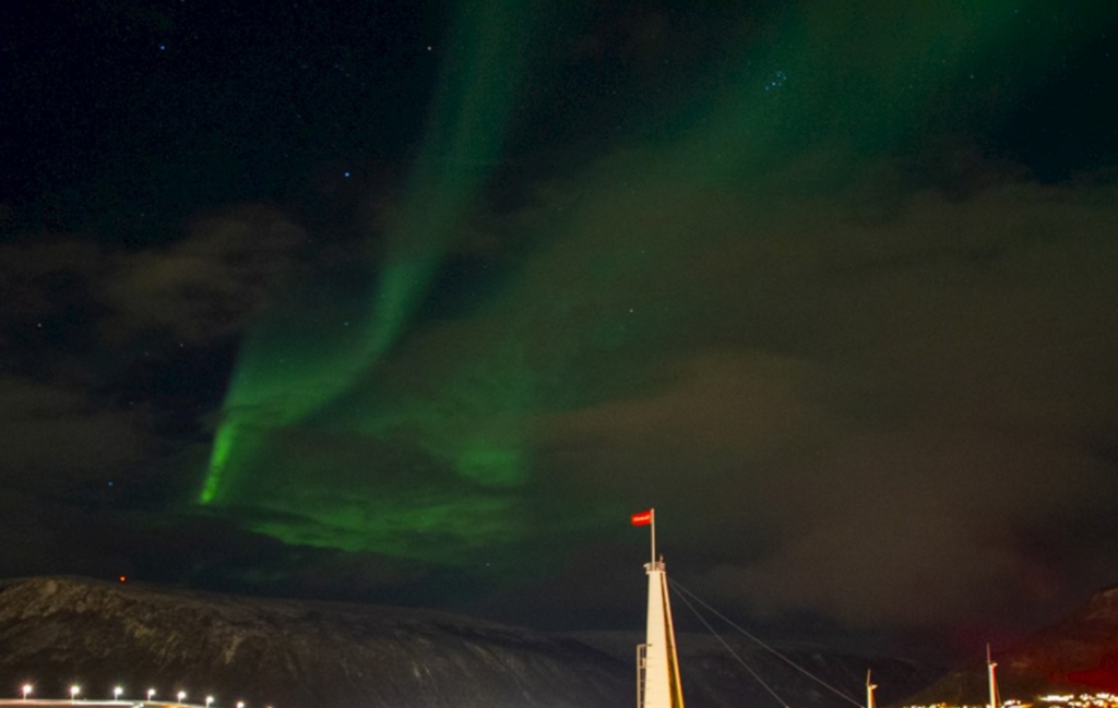 Groen noorderlicht boven de mast van zeilschip Antigua tijdens een groepsrondreis in Noorwegen.