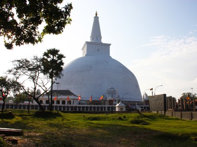 Witte Ruwanwelisaya-stoepa in Anuradhapura, Sri Lanka, met vlaggen en bomen op de voorgrond.