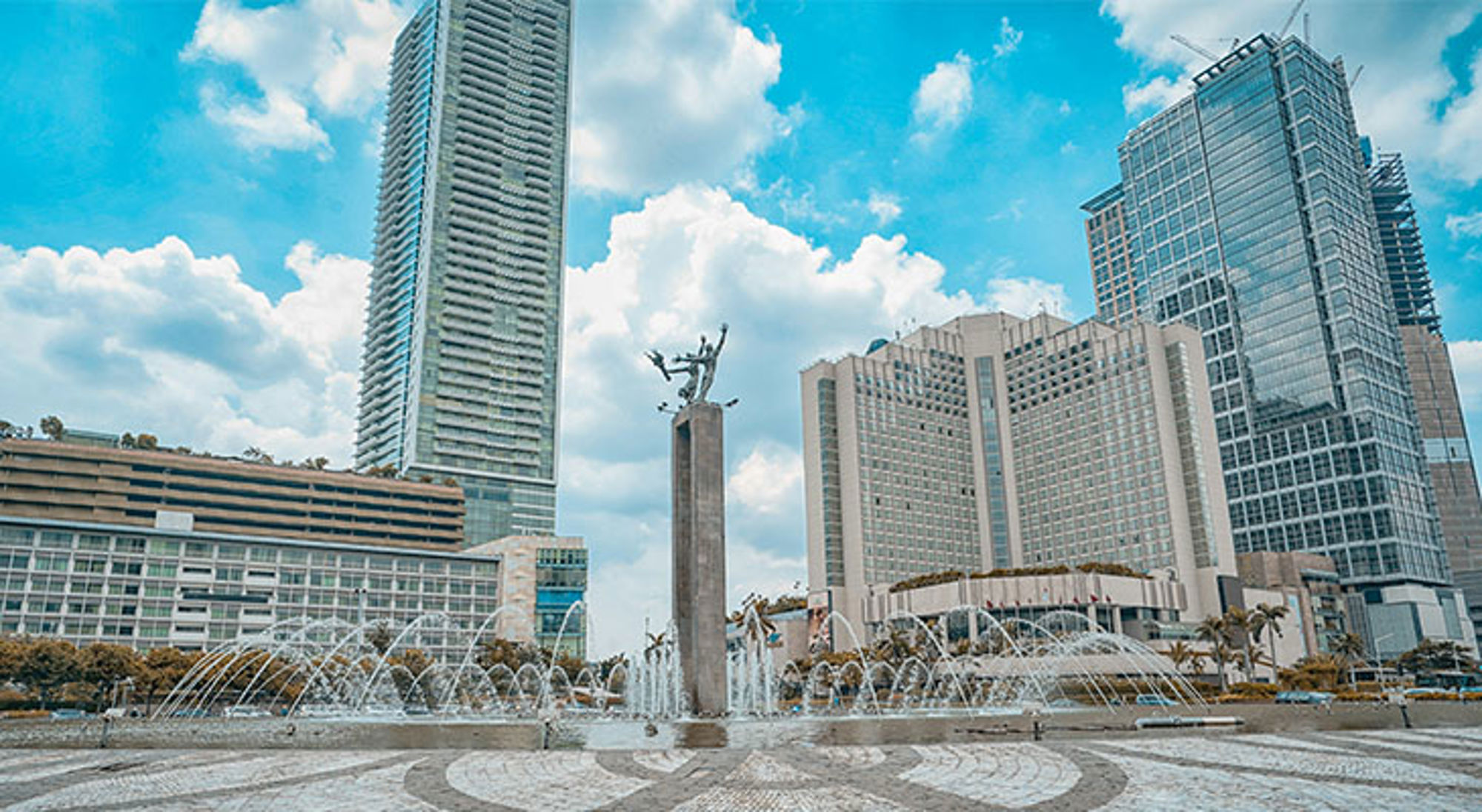 Monas-monument op Merdeka Square in Jakarta met fontein en wolkenkrabbers op de achtergrond.