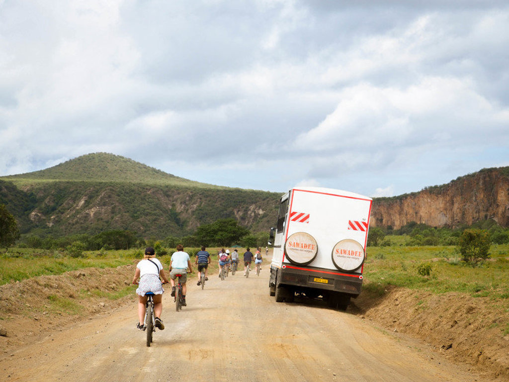 Groep fietsers tijdens 22-35ers reis Kenia & Tanzania op een zandweg langs bergen en savanne.