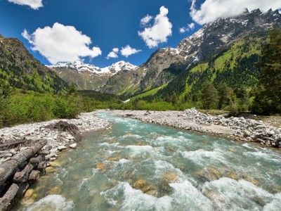Berglandschap in Georgië met snelstromende rivier, groene bossen en besneeuwde bergtoppen.