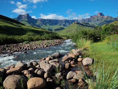 Rivier met rotsen in de Drakensbergen, met groene bergen en blauwe lucht op de route Johannesburg–Kaapstad.