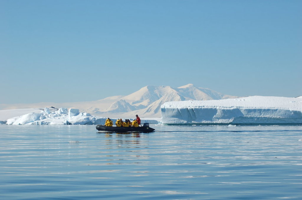 Zodiacboot met reizigers in Antarctica tussen ijsbergen en besneeuwde bergen tijdens groepsrondreis.