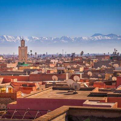 Uitzicht over de daken van Marrakech met minaret en het Atlasgebergte op de achtergrond.