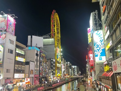 Avondbeeld van Dotonbori in Osaka met verlichte neonreclames langs het kanaal en een reuzenrad op de achtergrond.