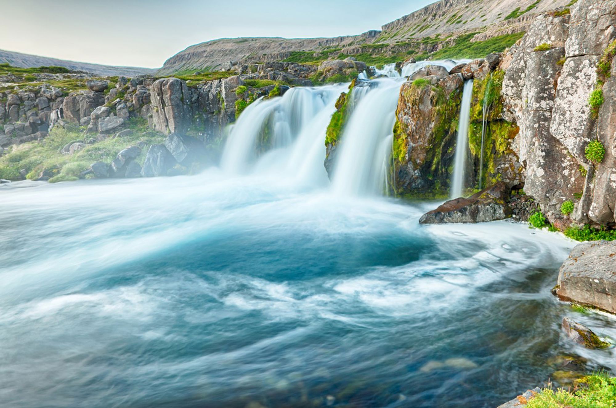 Waterval in IJsland die tussen rotsen in een helderblauwe rivier stroomt.