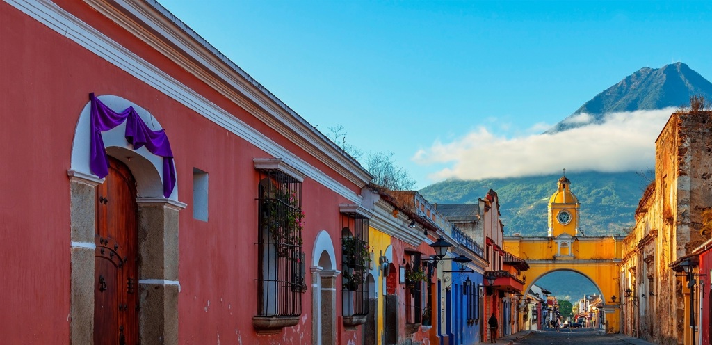Kleurrijke straat in Antigua, Guatemala met de Arco de Santa Catalina en de vulkaan Agua op de achtergrond.