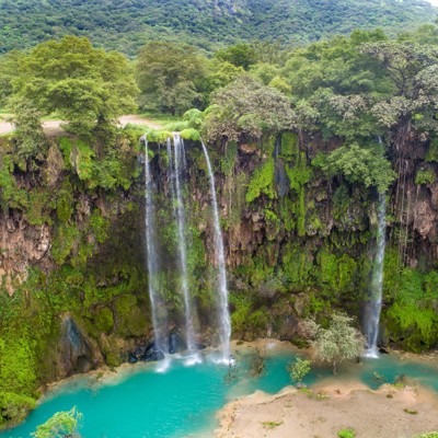 Waterval in een groene kloof met turquoise water, tijdens de groepsrondreis Oman en Dubai.