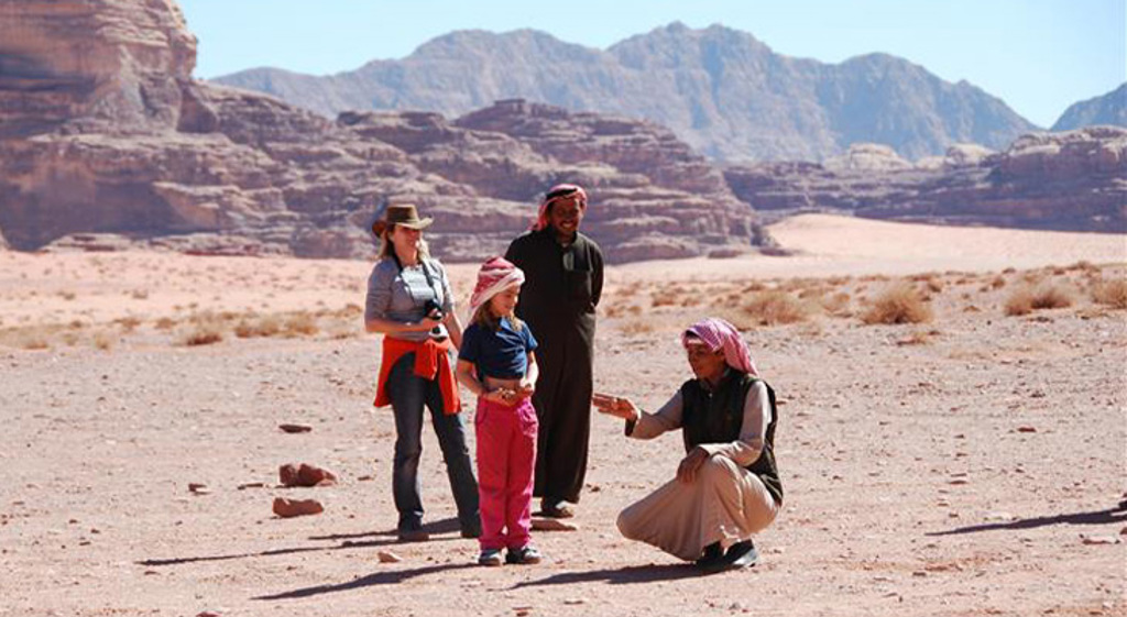 Gezin met lokale gids in de Wadi Rum-woestijn, Jordanië, met rotsformaties op de achtergrond.