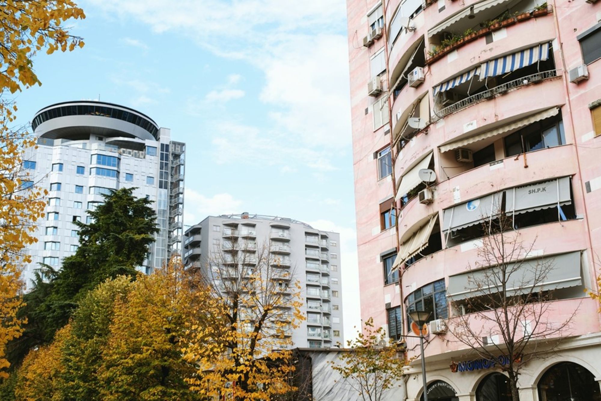 Moderne hoogbouw en appartementen in Tirana, Albanië, met herfstbomen op de voorgrond.
