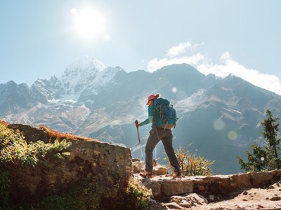 Wandelaar met rugzak op bergpad tijdens de Route Nepal Everest Base Camp, met besneeuwde Himalaya op de achtergrond.