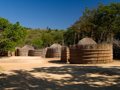 Traditionele bijenkorfvormige hutten in een Swazi-dorp, omringd door houten hekken en groene heuvels.